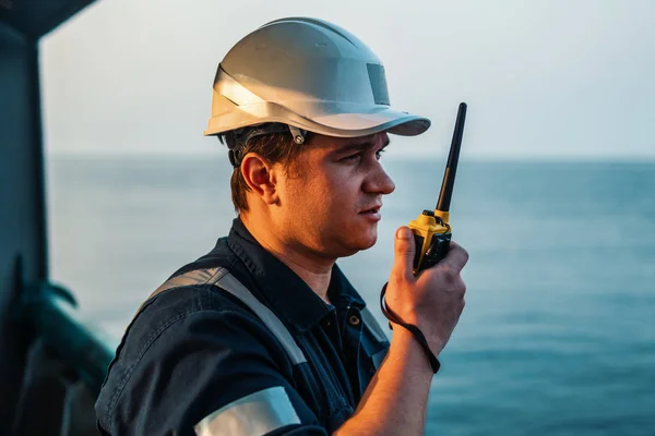 Officier de pont maritime ou second sur le pont d'un navire hauturier ou d'un navire, portant un équipement de protection individuelle EPI casque, combinaison. Il tient la radio VHF talkie-walkie dans les mains. — Photo