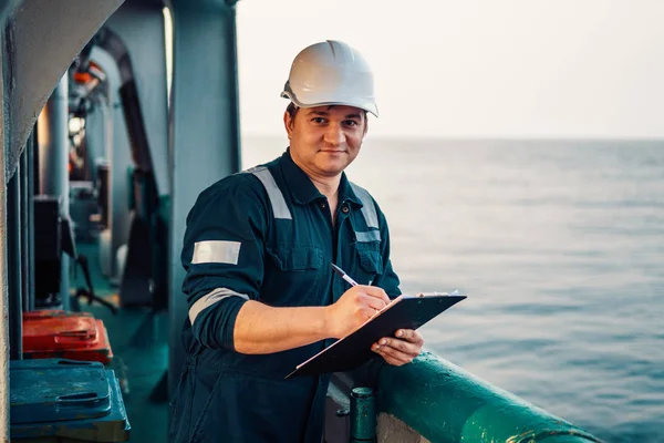 Oficial de convés no convés de embarcação ou navio offshore, usando equipamento de proteção individual EPI. Ele preenche a lista de verificação. Papelada no mar — Fotografia de Stock