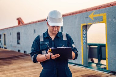 Güverte görevlisi offshore gemi veya gemi güvertede, PPE kişisel koruyucu ekipman giyiyor. Kontrol listesini doldurur. Denizdeki evraklar