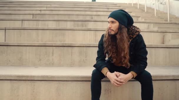 Portrait de hipster aux cheveux longs assis dans la rue dans la ville moderne — Video