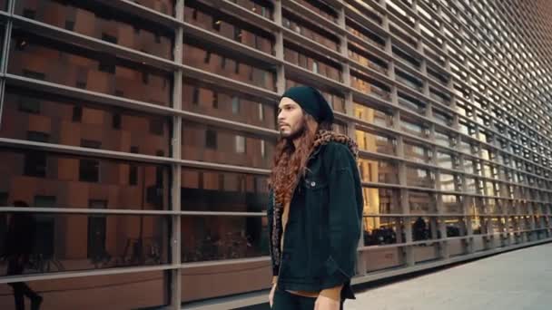 Retrato de hipster de pelo largo caminando por la calle en la ciudad moderna — Vídeo de stock