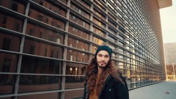 Портрет длинноволосого хипстера, идущего по улице в современном городе — стоковое видео