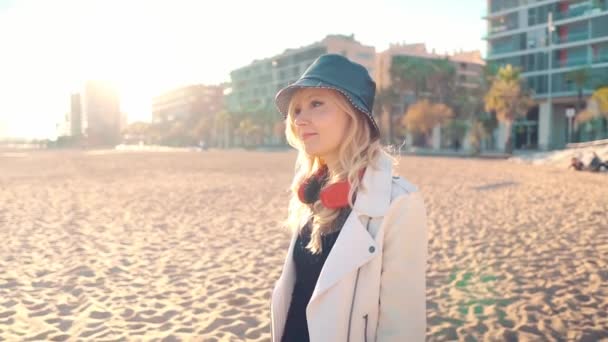 Γυναίκα περπάτημα κατά μήκος όμορφη παραλία στο ηλιοβασίλεμα με ακουστικά — Αρχείο Βίντεο