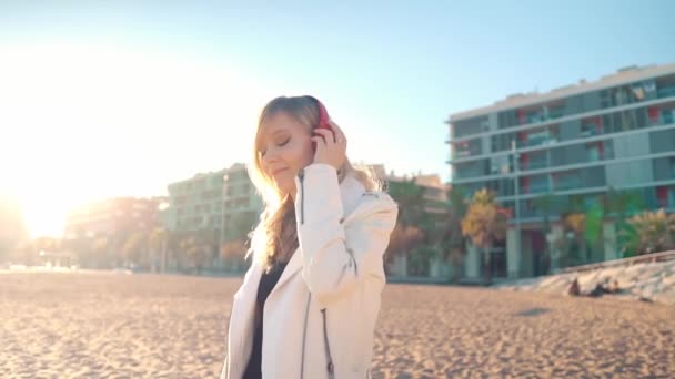 Vrouw wandelend langs prachtig strand bij zonsondergang met hoofdtelefoon — Stockvideo