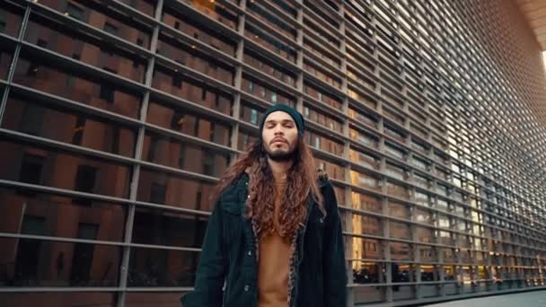 Retrato de hipster de pelo largo caminando por la calle en la ciudad moderna — Vídeos de Stock