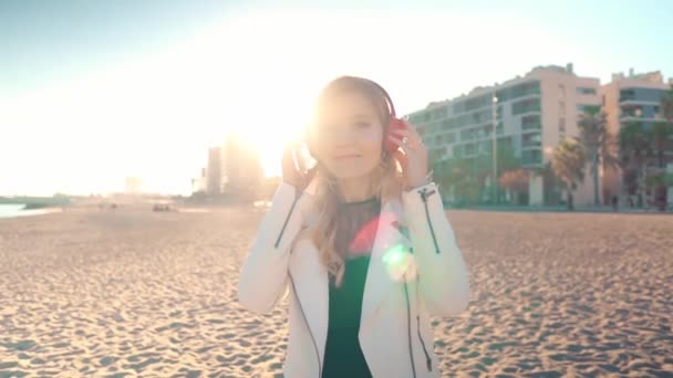 Vrouw wandelend langs prachtig strand bij zonsondergang met hoofdtelefoon — Stockvideo