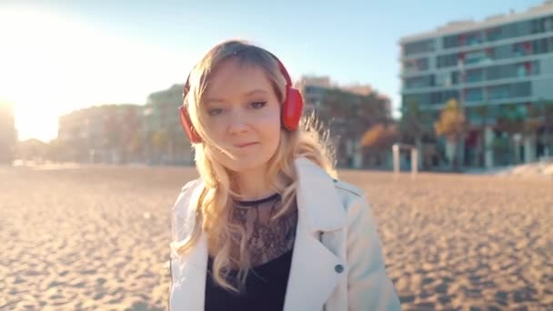 Жінка гуляє вздовж красивого пляжу на заході сонця з навушниками — стокове відео