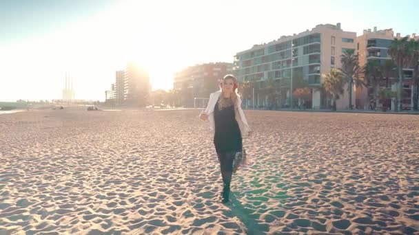 Mujer caminando por la hermosa playa al atardecer con auriculares — Vídeo de stock