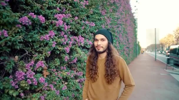 Портрет длинноволосого хипстера, идущего рядом с парком в современном городе — стоковое видео