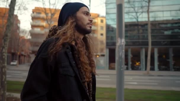 Portrét dlouhosrstého hipstera kráčejícího po ulici v moderním městě — Stock video