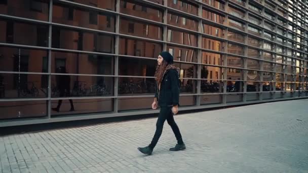 Портрет длинноволосого хипстера, идущего по улице в современном городе — стоковое видео