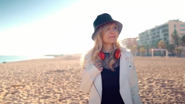 Woman walking along beautiful beach at sunset with headphones — 비디오