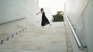 Siyah elbiseli genç profesyonel balerin dışarıda dans ediyor.