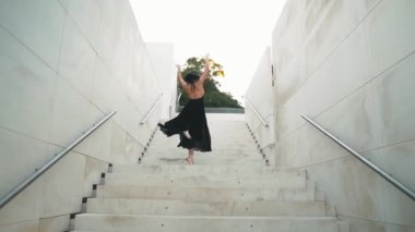 Siyah elbiseli genç profesyonel balerin dışarıda dans ediyor.