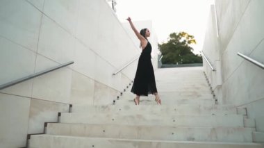 Siyah elbiseli genç profesyonel balerin dışarıda dans ediyor.