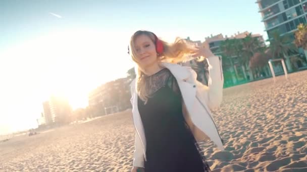 Gün batımında güzel kumsalda yürüyen bir kadın kulaklıkla — Stok video