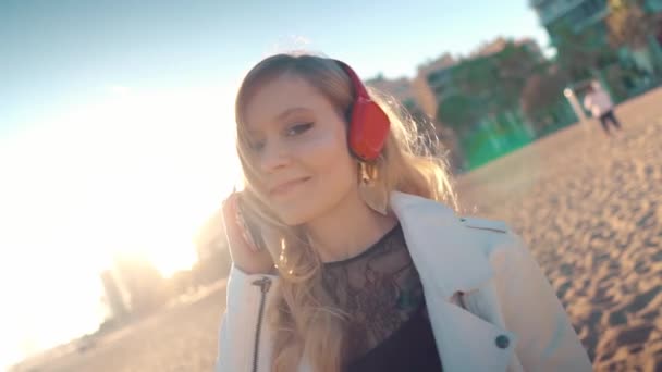 Vrouw wandelend langs prachtig strand bij zonsondergang met hoofdtelefoon — Stockvideo