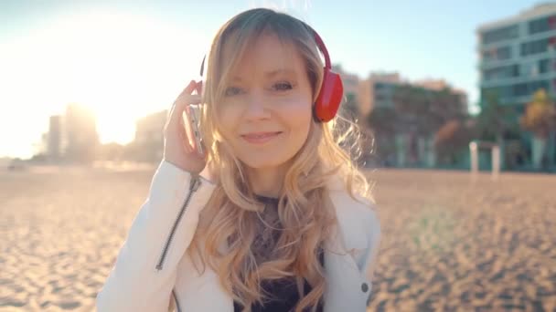 Gün batımında güzel kumsalda yürüyen bir kadın kulaklıkla — Stok video