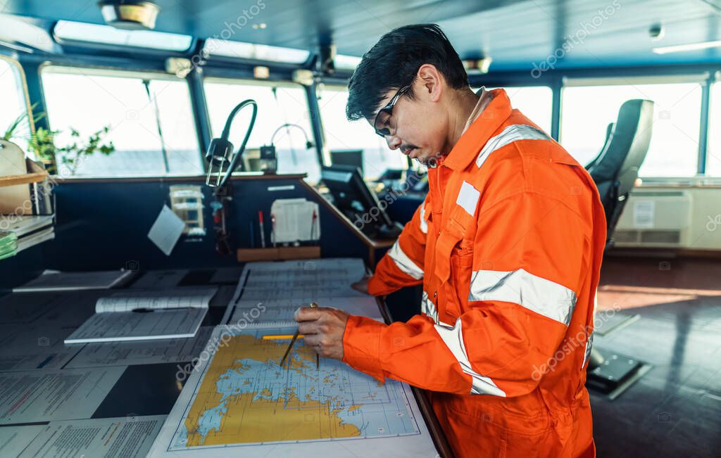 Filipino deck Officer on bridge of vessel or ship. He is plotting position on chart