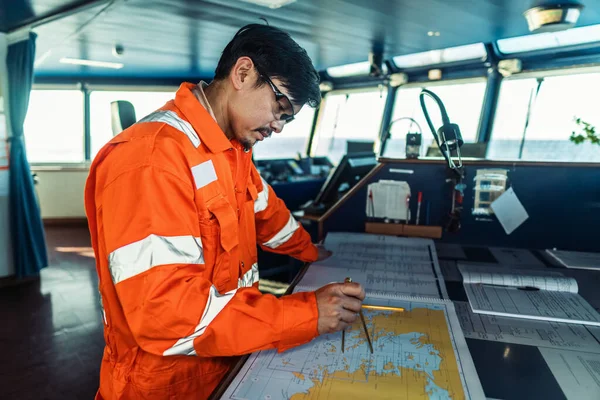 Filipino deck Officer on bridge of vessel or ship. He is plotting position on chart