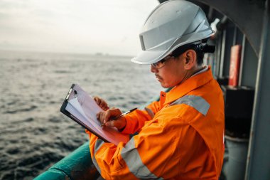 Filipinli güverte subayı kıyı gemisinin güvertesinde kontrol listesini dolduruyor. Denizdeki evrak işleri.