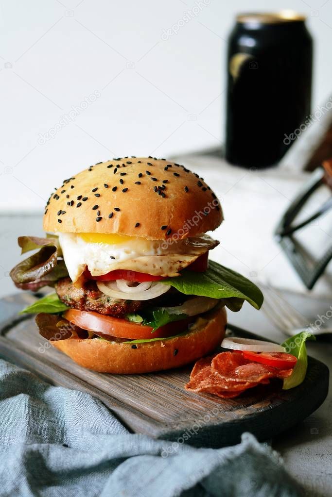 A large burger with a cutlet, vegetables, egg and a fresh roll. Sandwich for breakfast. Fast food. Men's Food.