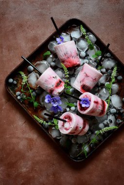 Kremalı dondurma siyah frenk üzümü, böğürtlen, ahududu, nane ve menekşe koyu arka plan üzerinde çiçekler meyveler. Yaz soğutma tatlı. Ev yapımı dondurma veya çubuklu dondurmayı yeşil nane bırak dekore edilmiş