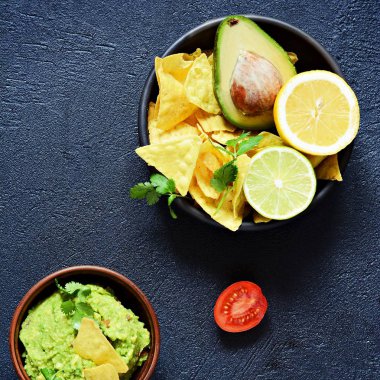 Bir kase Meksika mezesi sosu, mısır cipsi (cips) ve siyah arka planda malzemeler, seçici odaklanma. Meksika ulusal yemeği.