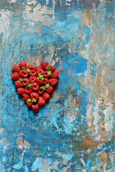 Heart shape made of premium raspberries on a blue background. Close up, top view, high resolution product. Romantic concept. Valentine\'s day symbol