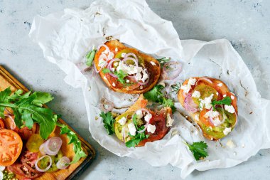 İtalyan bruschetta (sandviç, crostini, tapas, tost) taze domates, ricotta, otlar, soğanlar, zeytinyağı ve roka yapraklarıyla mavi bir zemin üzerinde. Geleneksel İtalyan aperatifi veya aperatifi, antipasto.