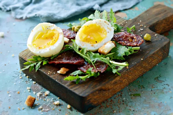 松软煮熟的鸡蛋 早餐用什锦香肠 新鲜的牛油果沙拉和饼干放在蓝色背景的木板上 — 图库照片