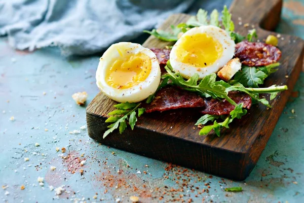 松软煮熟的鸡蛋 早餐用什锦香肠 新鲜的牛油果沙拉和饼干放在蓝色背景的木板上 — 图库照片