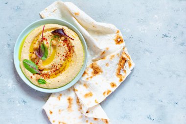 İçinde otlar, tütsülenmiş kırmızı biber, zeytinyağı ve mavi (gri) arka planda marul bulunan klasik humus. Sağlıklı vejetaryen yemeği. Bir tabak Orta Doğu mutfağı. Sağlıklı yeme kavramı.