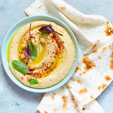 İçinde otlar, tütsülenmiş kırmızı biber, zeytinyağı ve mavi (gri) arka planda marul bulunan klasik humus. Sağlıklı vejetaryen yemeği. Bir tabak Orta Doğu mutfağı. Sağlıklı yeme kavramı.