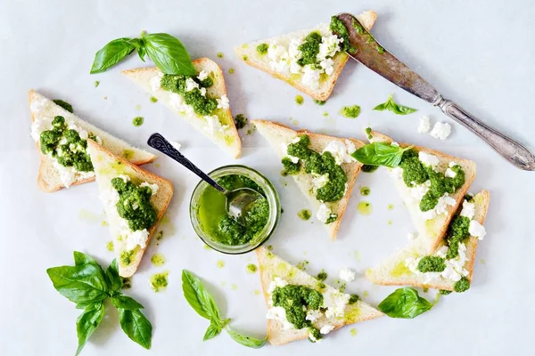 Kızarmış ekmek (crostini, bruschetta), süzme peynir (ricotta) ve taze hazırlanmış pesto. Ev yapımı fesleğen pekhto sosu kavanozda hafif arka planda..