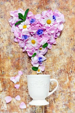 Kahverengi arka planda gül yaprakları serpiştirilmiş beyaz seramik bardak. Gül yapraklarının kalbi.