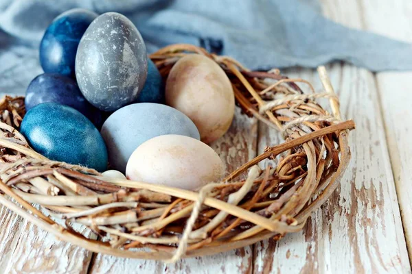 Colored easter eggs in wicker basket on a light wooden background. Easter basket.