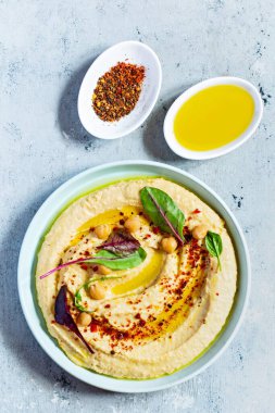 İçinde otlar, tütsülenmiş kırmızı biber, zeytinyağı ve mavi (gri) arka planda marul bulunan klasik humus. Sağlıklı vejetaryen yemeği. Bir tabak Orta Doğu mutfağı. Sağlıklı yeme kavramı.