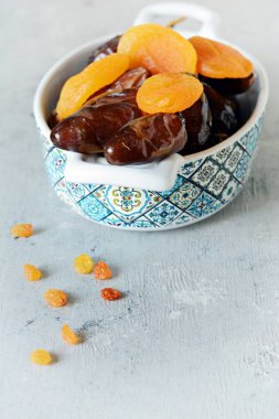 Dalında sulu tarihler olan kaseler ve gri-mavi arka planda kurutulmuş kayısılar. Sağlıklı lezzetli yemekler, atıştırmalıklar.