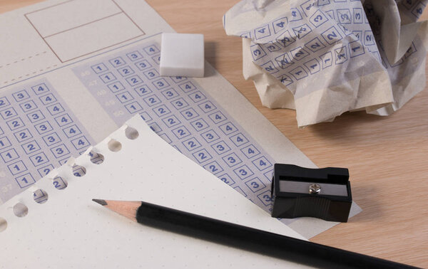 Crumpled paper ball of vintage classic answer sheet with pencil, sharpener and paper reduction. Cross the right answer in the box with blank answer. Answer sheet concept.