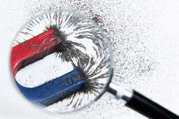 Magnet menarik kekuatan besi dengan kekuatan magnetik melalui kaca pembesar. Percobaan ilmiah di kelas sains di sekolah . — Stok Foto