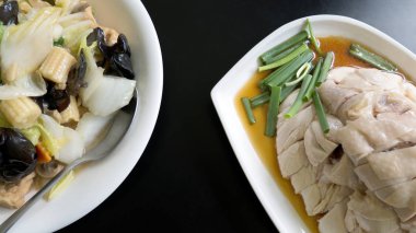 Hainanese tavuk pirzola ve beyaz plaka üzerinde siyah tablo arka plan üzerinde tavada kızartılmış karışık sebze. En sevdiğim Çin ana yemek tarifleri.