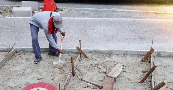 Neidentifikovaný pracovník pracuje kope díru s shvel a rýč v písku na silnici staveniště. Koncepce výstavby silnice. — Stock fotografie