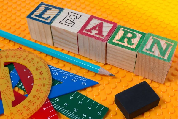 Lär dig ord skrivet i trä kub gul plast med skolan brevpapper verktyg. — Stockfoto