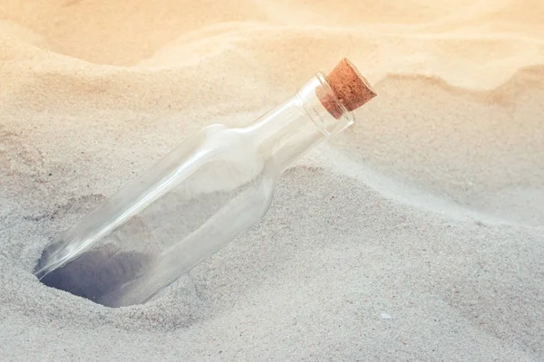 Old vintage empty glass bottle with natural tapered cork lid on the sand beach close-up.