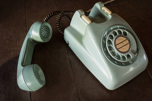 Old green vintage telephone, phone land  or landline with dust on wooden retro desk.