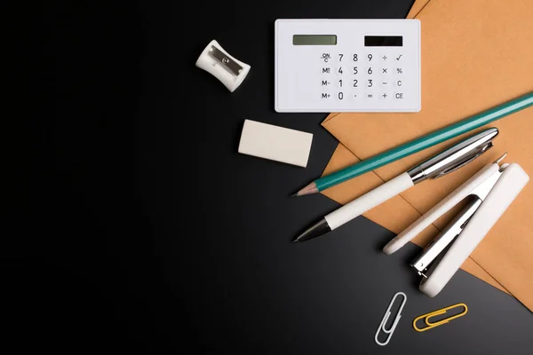 Mesa de escritorio de oficina con lápiz de suministros de oficina, borrador, sacapuntas, sobre y calculadora en papel de oficina negro . — Foto de Stock