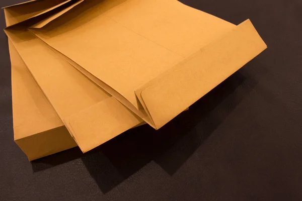 Blank envelopes on a dark leatherette background texture. Back side of yellow envelopes on dark brown wooden table. Envelopes for business concept. — Stock Photo, Image