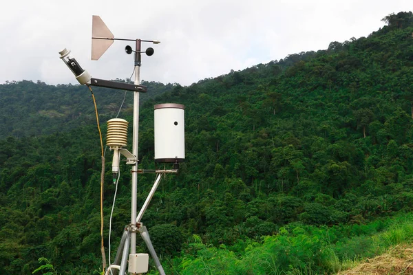 Meteorological weather station antenna with meteorology sensors, pale overcast cloudy sky and forest in background. Weather station for background.