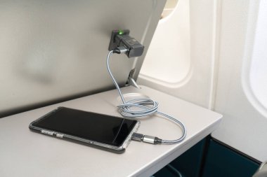 Uçak yolcusu uçuş sırasında şarj aletini akıllı telefon olarak kullanıyor. Uçaktaki şarj istasyonu..